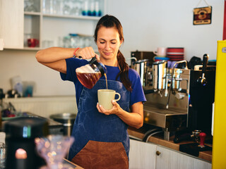 Barista pouring coffee into a cup at a cozy café in the morning light, showcasing skillful brewing...