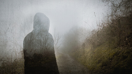 A double exposure of a ghost like hooded figure. Standing on a spooky country path in winter, With...