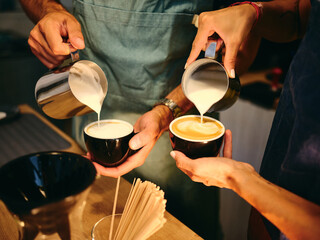 Baristas skillfully pour steamed milk into cups at a cozy café during a sunny morning