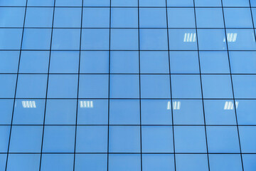 the facade of a modern building made of glass as a background, a reflection of the blue sky