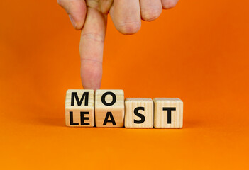 Most or least symbol. Businessman turns beautiful wooden cubes and changes the word Least to Most. Beautiful orange table orange background. Copy space. Business and most or least concept.