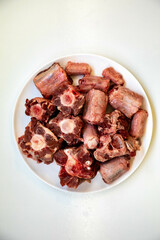 Raw beef oxtail on a round white plate in closeup.