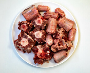 Raw beef oxtail on a round white plate in closeup.