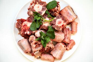 Raw beef oxtail on a round white plate in closeup.