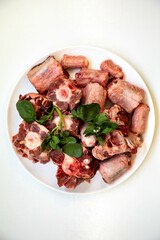 Raw beef oxtail on a round white plate in closeup.