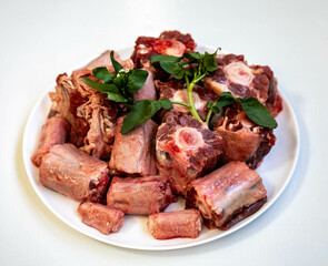 Raw beef oxtail on a round white plate in closeup.