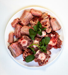 Raw beef oxtail on a round white plate in closeup.