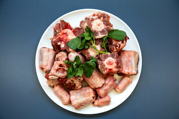 Raw beef oxtail on a round white plate in closeup.
