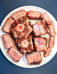 Raw beef oxtail on a round white plate in closeup.