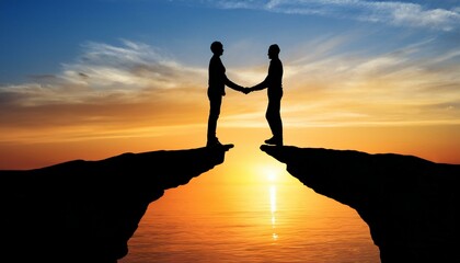 Against a vibrant sky, two silhouettes are shaking hands over a gap on a cliff at sunset.