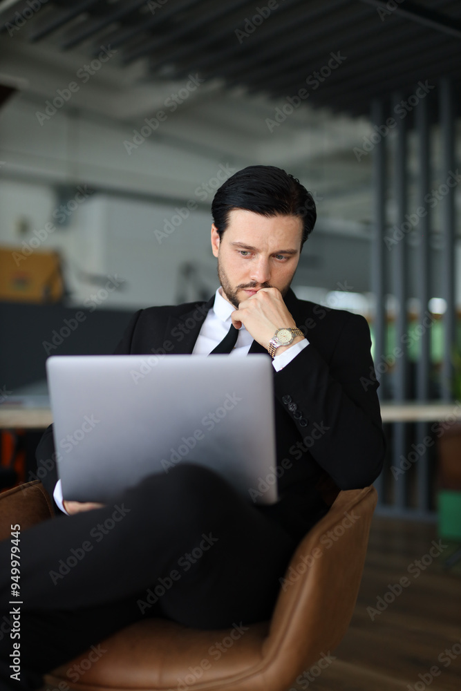 Poster a man in a suit is sitting in a chair with a laptop open in front of him. he is deep in thought, pos