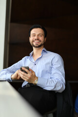 A man is sitting at a table with a cell phone in his hand. He is smiling and he is happy