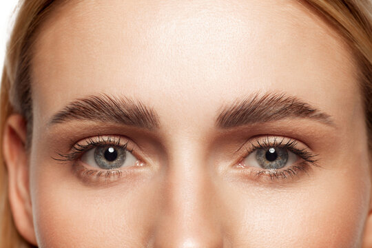 Close-up of beautiful clear female face with attractive gray eyes, perfect eyebrows and natural lashes. Eyebrow and lash lamination. Concept of makeup, cosmetics, natural beauty, skin care products