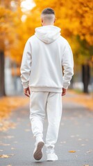 Obraz premium A man with a shaved head and a simple, casual outfit, including a hoodie and sweatpants, walking through a quiet street, representing a minimalist approach to fashion and grooming