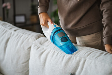 Unknown woman stand and vacuuming sofa with hand vacuum cleaner