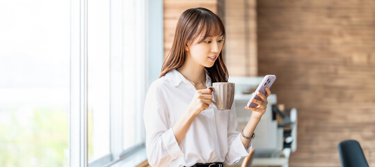 飲み物を飲みながらスマホを見る笑顔のビジネスウーマン