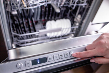 Woman's hand turns on the dishwasher to wash the dishes. Built-in appliances in the kitchen.