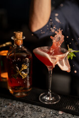 A cocktail splashing out of the glass next to a Bumbu rum bottle, showcasing motion and energy. Dark, moody lighting.