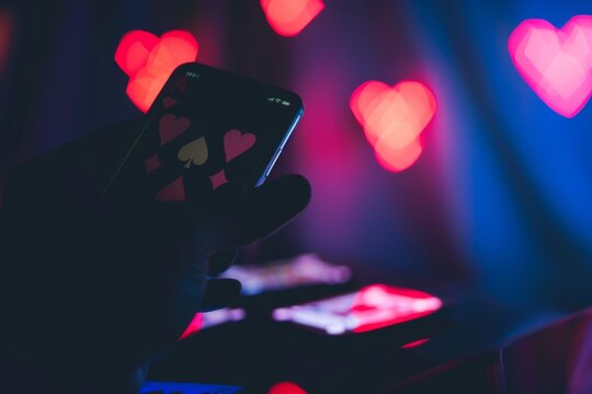A person is holding a cell phone with a heart design on it. The phone is in a dark room with a red background
