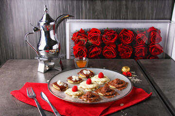 Romantic mix Mini Pancake Platter topped with chocolate, white chocolate, raspberries, almonds, and chocolate candy balls with arabic coffee served in plate isolated on napkin side view of dessert
