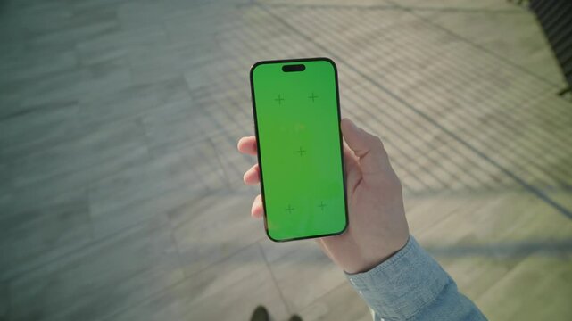 Man hands holding and scrolling vertically phone with green screen. On background road at sunlight. Typing on smartphone