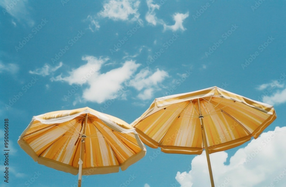 Wall mural two yellow beach umbrellas against a bright blue sky with fluffy white clouds a cheerful summer atmo