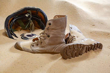 An arrangement of abandoned military gear, including a worn-out boot, helmet, and shattered...