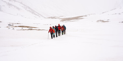 A group of people walking on the snowy mountains with their snowshoes on. Climbing the icy mountains
