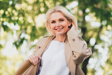 Portrait of charming lovely pensioner lady spring walking touch hair good mood wear beige coat enjoy free time weekend outdoors