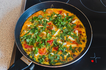 A vibrant omelette filled with fresh herbs and vegetables cooks to perfection in a sleek frying pan on the stove.