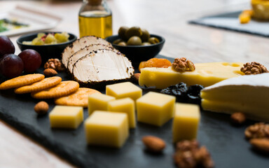 Cheese plate with grapes, nuts, olive and olive oil on dark stone board.