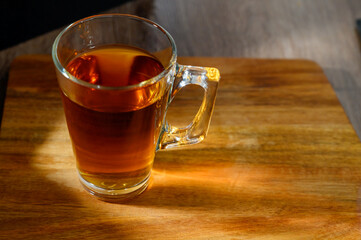 Black tea leaves floating in clear hot water in a glass cup on a wooden table