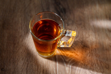 A clear glass cup of tea infused steaming on a wooden table