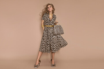 Stylish female model wearing a fashionable leopard-print dress is posing on a beige background in the studio.