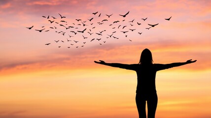 Fototapeta premium A person stands against a vibrant sunset, arms outstretched, as birds fly freely in the sky, embodying freedom and serenity.