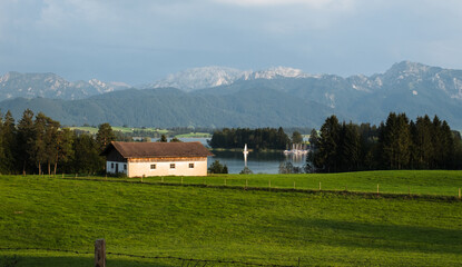 Landschaftsbild mit Bauernhof, See, Berge und grüner Wiese im Herbst