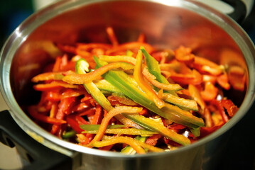 Close-up of red, yellow, and green bell pepper slices in a stainless steel pot, ready for cooking, with vibrant colors and fresh textures. 