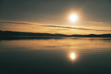 Sunrise over a Swedish lake with mirror-smooth water in front of trees on the shore