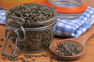 Lentilles du Puy sèches dans un bocal en verre avec une cuillère en bois en gros plan.
