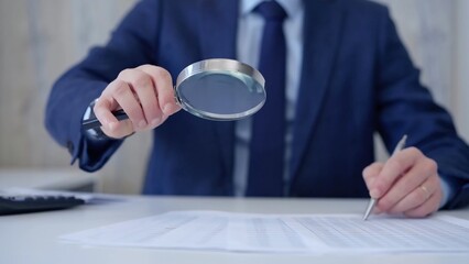Businessman is carefully examining financial documents with a magnifying glass, highlighting the importance of thorough analysis in business. Audit and taxes
