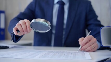 Businessman is carefully examining financial documents with a magnifying glass, highlighting the importance of thorough analysis in business. Audit and taxes