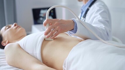 Naklejka premium Doctor man, wearing white medical gloves, is using ultrasound equipment on the breast of a female patient lying down for a medical cardiology examination. Medicine concept