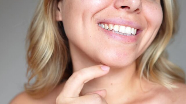 Young caucasian smiling blonde woman with wavy hair showing dimples on her cheeks on a dark grey background. Close-up of a blonde girl with even white teeth and beautiful smile