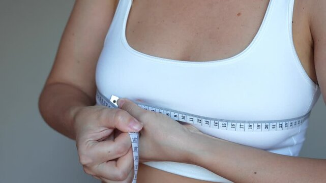 Young woman measuring the chest circumference with a measure tape on a grey background. Diet, sport healthy lifestyle, wellness concept