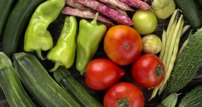 Asortment of freshly harvested vegetables from an organic garden: zucchini, cubanelle chilis, tomatoes, japanese cucumbers, bitter melons, tomatillos, runner bean, and green bean. Table spin.