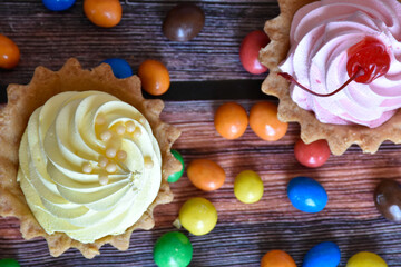 Colorful tartlets cakes with protein cream, multicolored dragee candies on wooden table. Delicious...