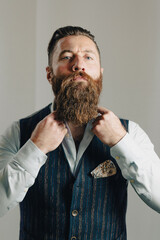 Bearded businessman buttoning up his waistcoat in studio portrait