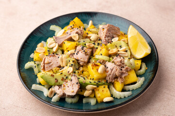 Salad with canned tuna, peanuts, mango, avocado, celery, chili flakes and black sesame. Light summer salad with olive oil and a lemon lobule. Home cooking. Selective focus, close-up.
