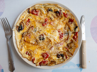 An open or flat omelette with tomatoes, mushrooms, onions and cheese, served on a plate.
