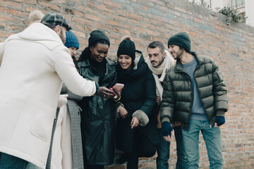 Group of young people using phone together outside in winter